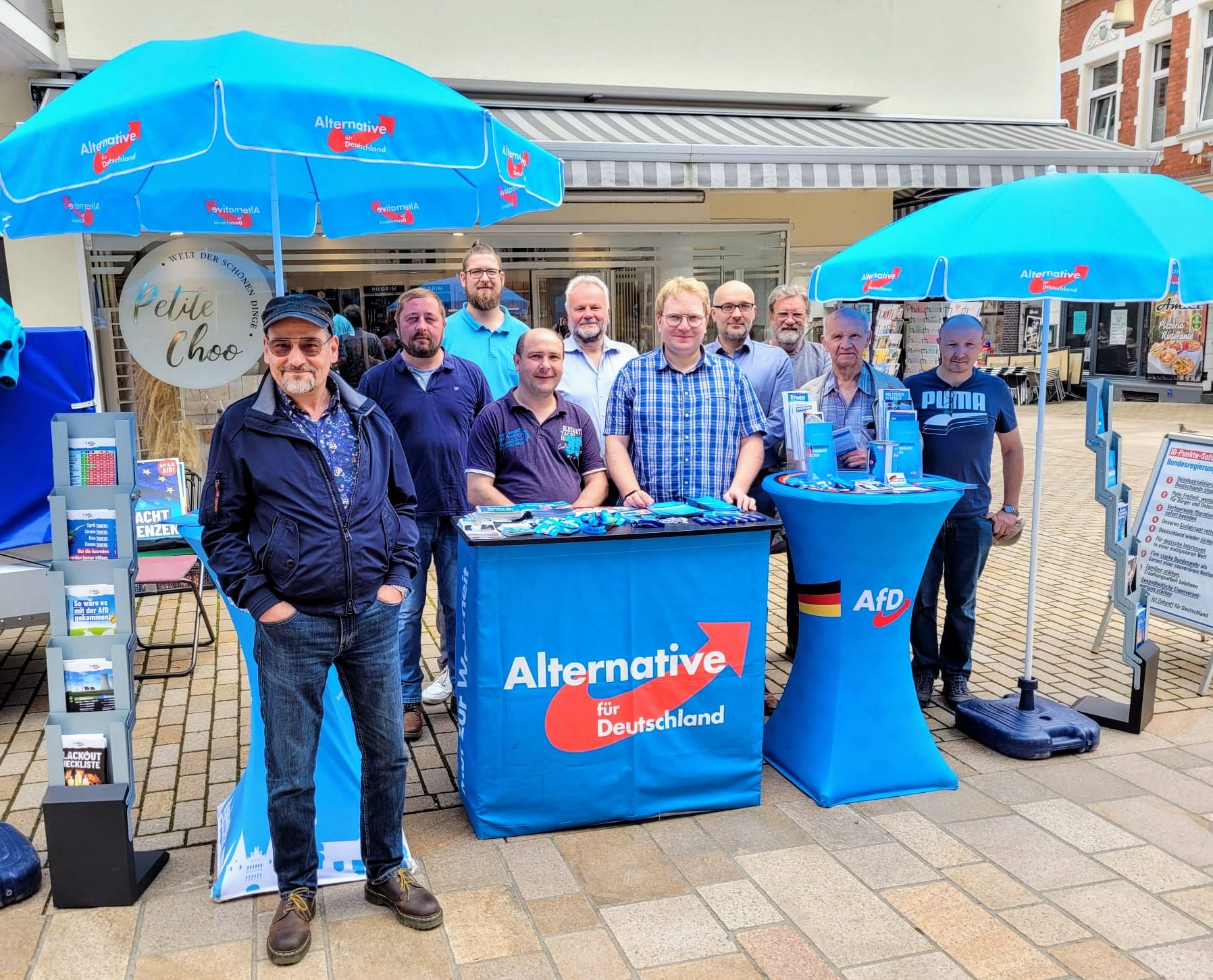 Gruppe von zehn Männern an einem Informationsstand der AfD in einer Fußgängerzone.